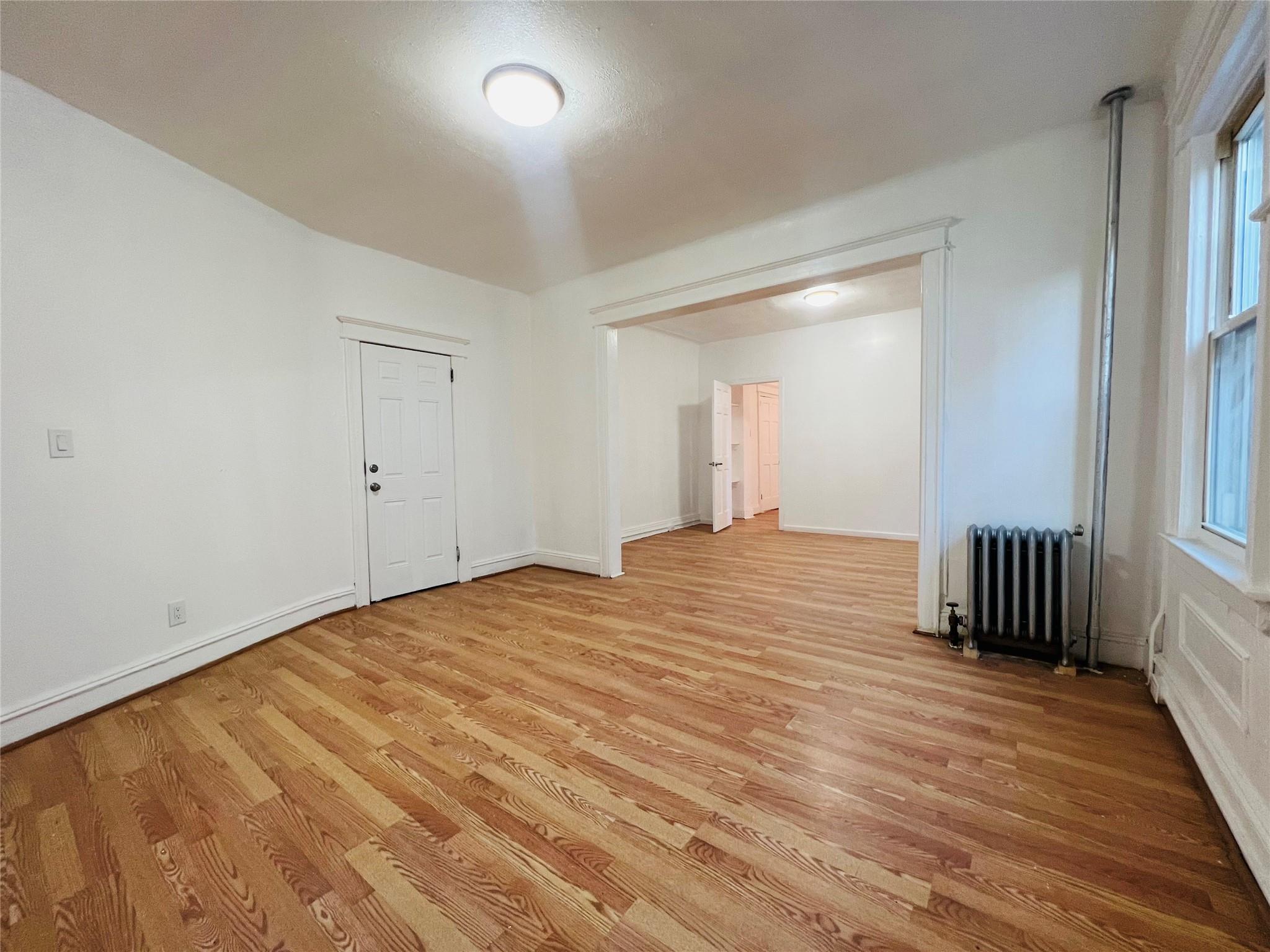 Empty room with light wood-type flooring and radiator