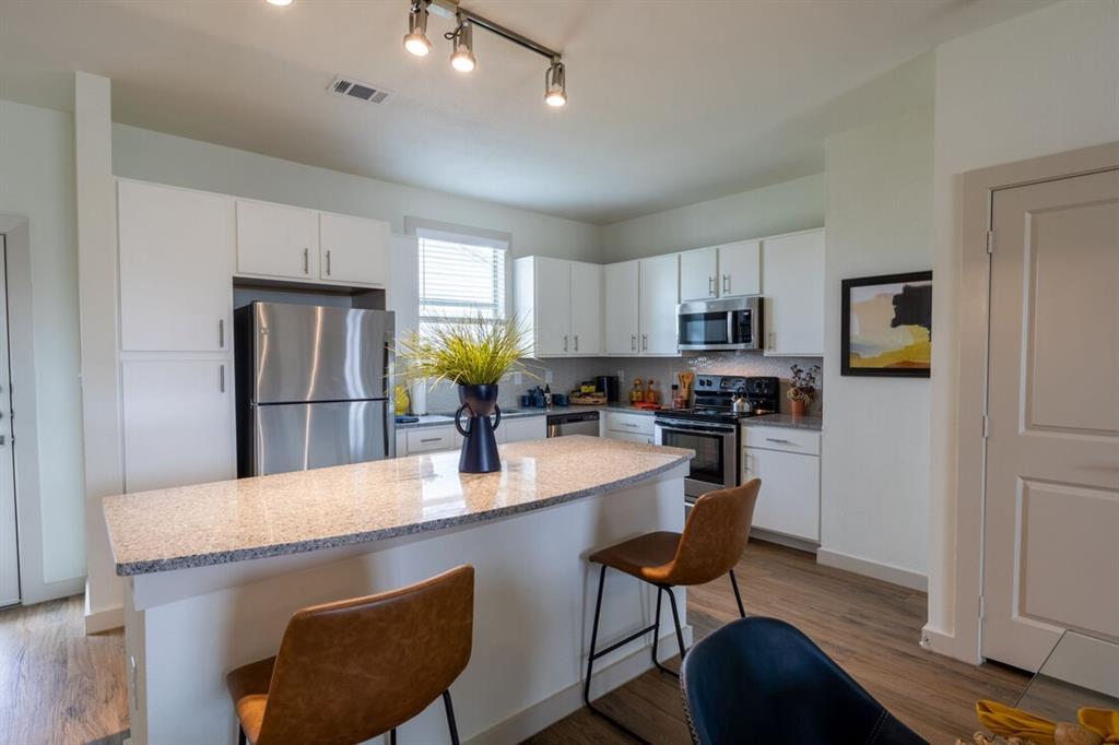 a kitchen with stainless steel appliances granite countertop a stove a refrigerator a kitchen island a sink dishwasher and white cabinets with wooden floor