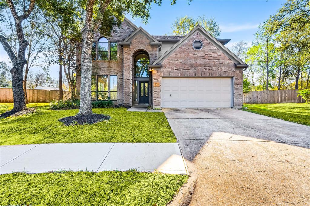 Sunlight dances across the warm brick facade of this stunning two-story home, highlighting the arched windows and inviting front porch. The spacious driveway and lush landscaping surrounding the property complete this idyllic scene.