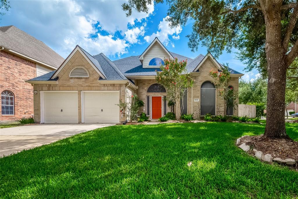 Spacious Two-Story Brick Home with a Two-Car Garage, a Well-Manicured Lawn with Mature Trees, and an Inviting Orange Front Door.