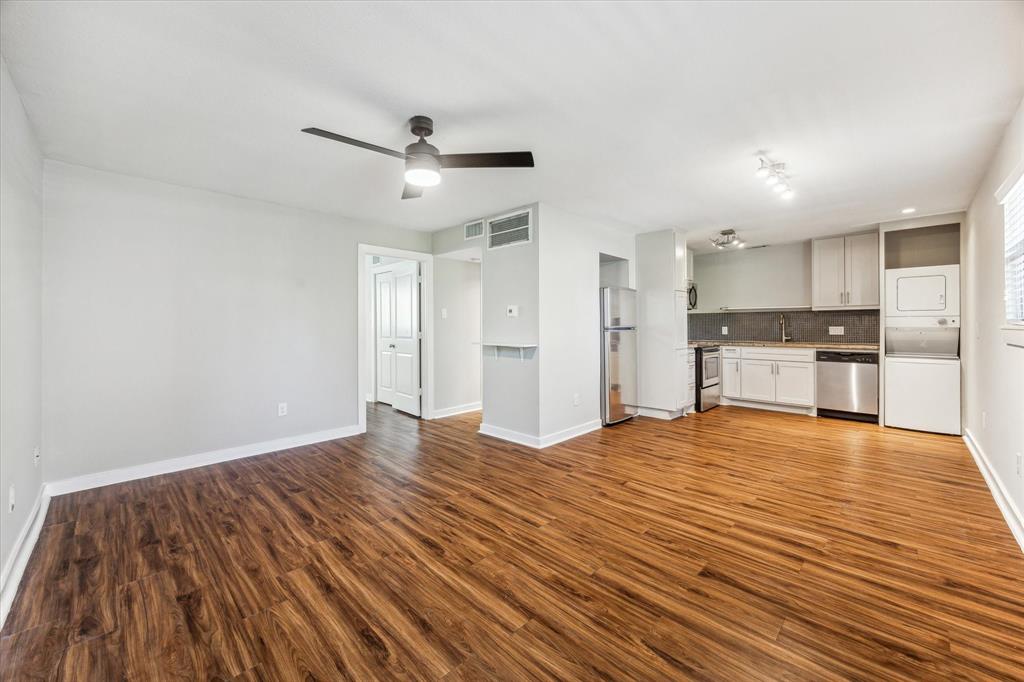 a view of empty room with wooden floor and kitchen view