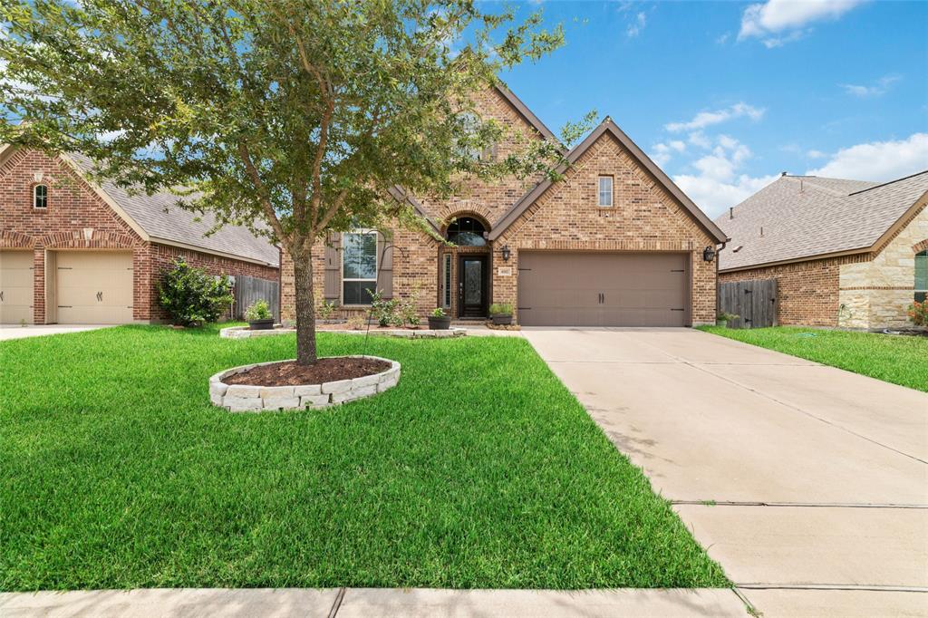 This is a well-maintained single-story brick home featuring a two-car garage, a neatly manicured lawn with mature tree, and an inviting entryway.