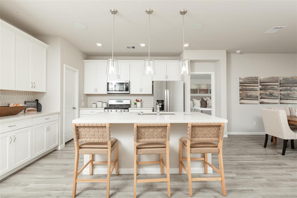 a kitchen with a dining table chairs wooden floor cabinets and appliances