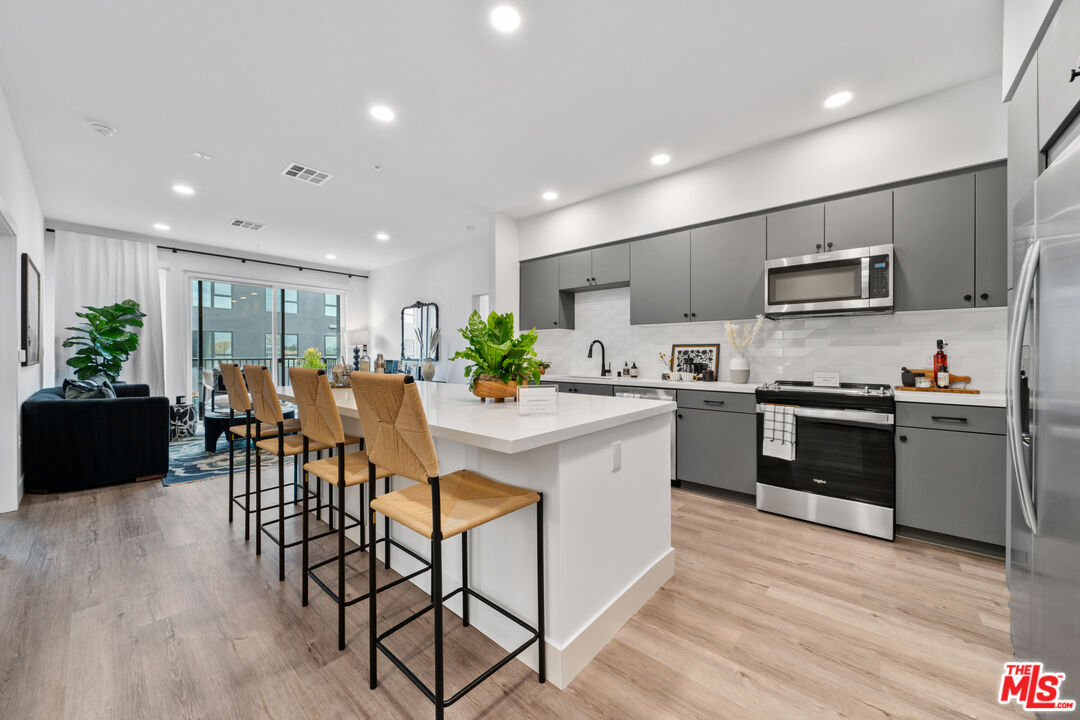 a kitchen with stainless steel appliances kitchen island granite countertop a stove top oven a sink a dining table and chairs with wooden floor