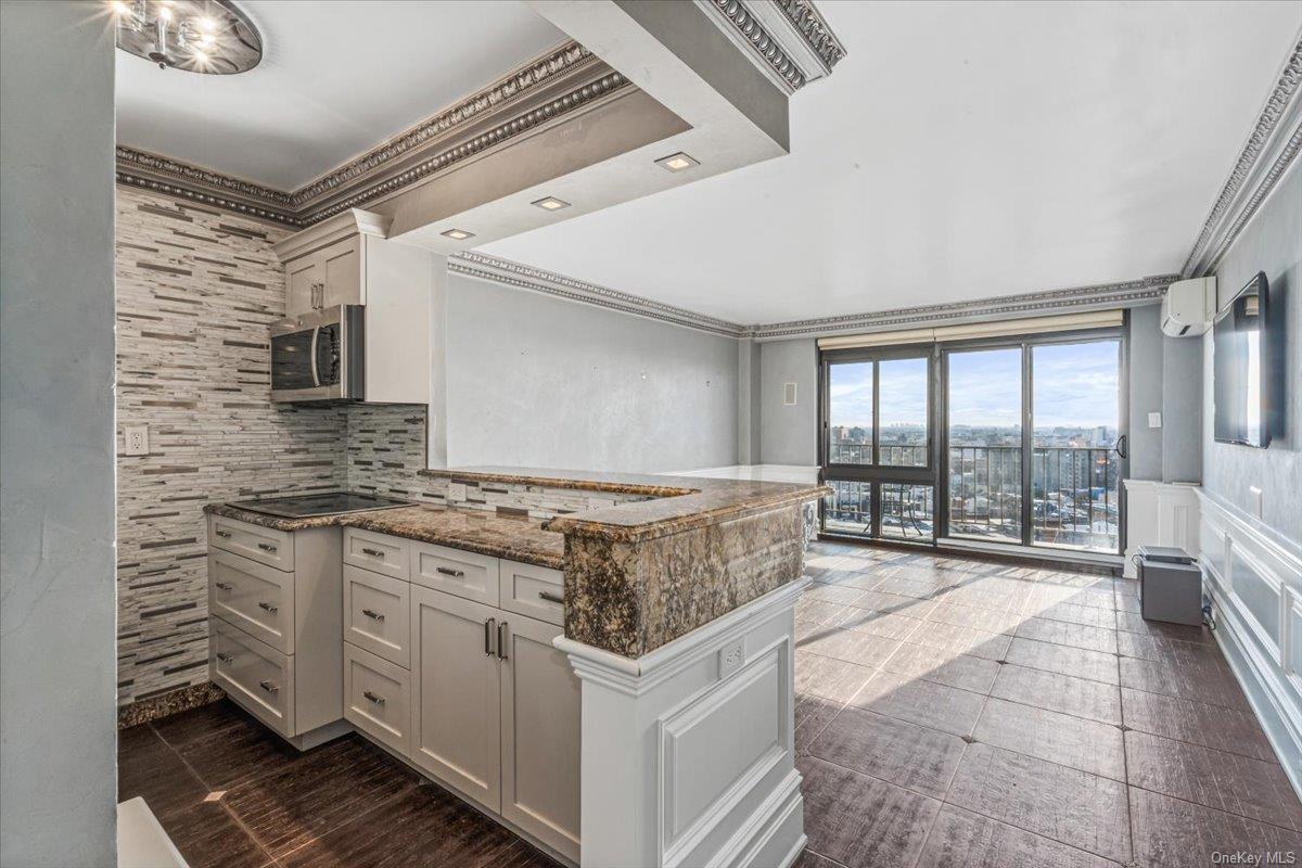 Kitchen featuring tasteful backsplash, white cabinetry, dark stone counters, and crown molding