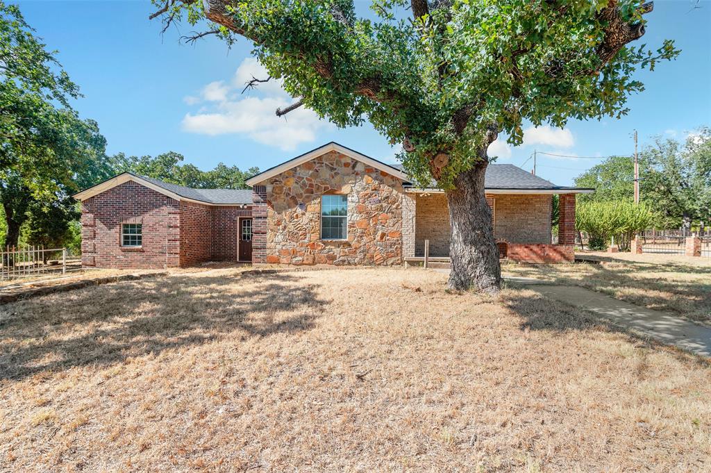 a front view of a house with a dirt yard and a large tree