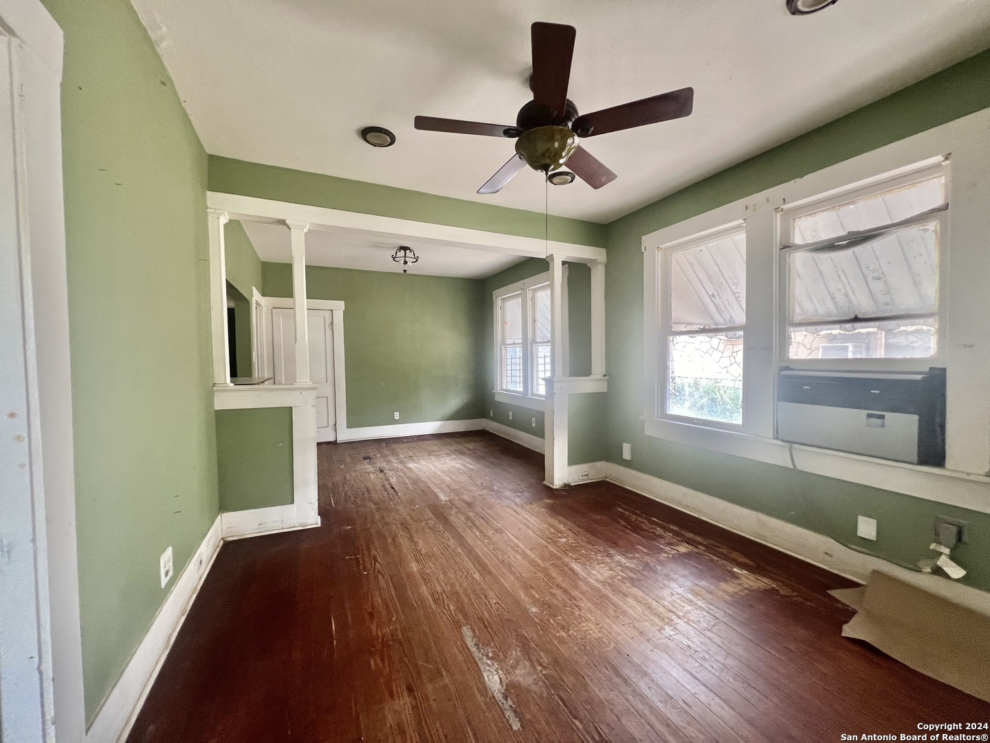 a view of a livingroom with wooden floor a ceiling fan and windows