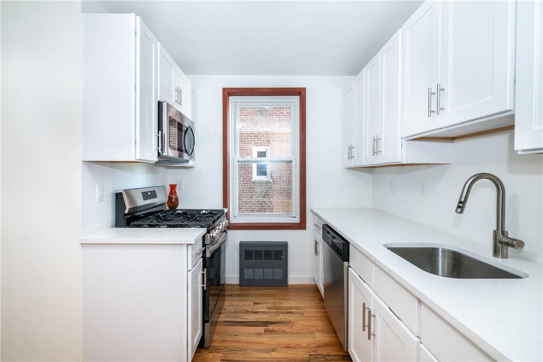 light hardwood / wood-style flooring, sink, appliances with stainless steel finishes, and white cabinetry