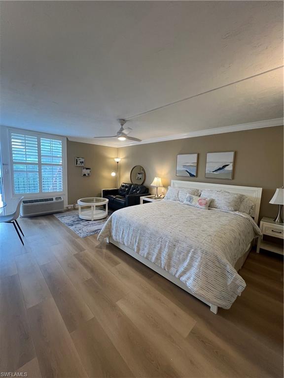 Bedroom with crown molding, a wall mounted AC, wood-type flooring, and ceiling fan