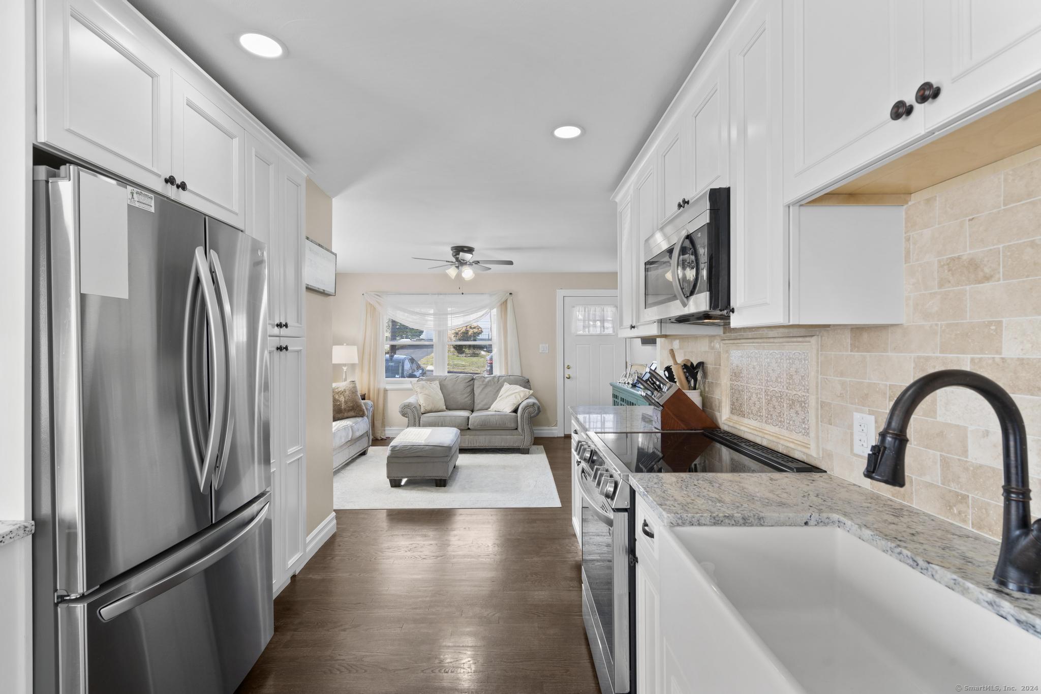 a kitchen with refrigerator a sink a stove and white cabinets with wooden floor