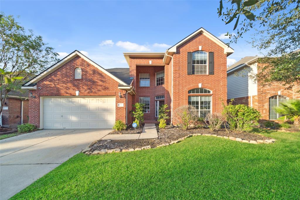 This is a two-story, brick-facade home featuring a double-height entry with large windows, a well-maintained lawn, and an attached two-car garage. The property is nestled in an established golf course neighborhood.