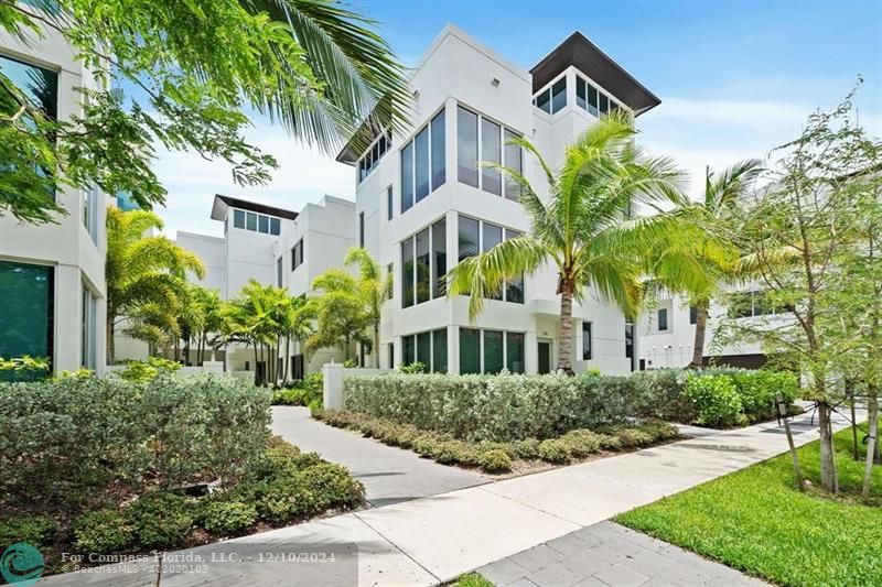 a front view of a multi story residential apartment building with yard and parking