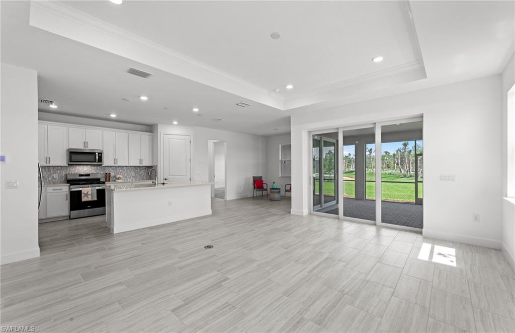 Kitchen featuring a tray ceiling, a center island with sink, backsplash, white cabinets, and appliances with stainless steel finishes