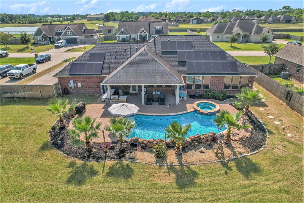 Spacious single-story home with a large backyard, in-ground pool, and covered patio area, flanked by palm trees and a privacy fence.