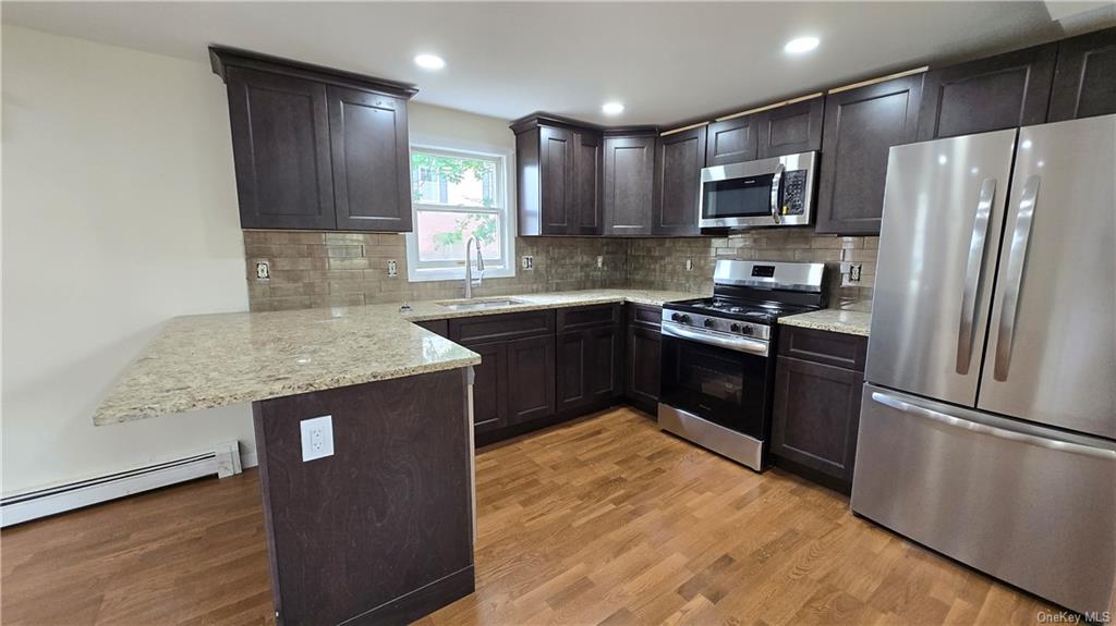 Kitchen with light wood-type flooring, stainless steel appliances, sink, kitchen peninsula, and tasteful backsplash