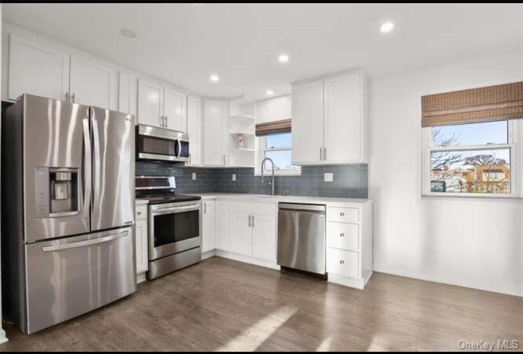 Kitchen featuring white cabinets, dark hardwood / wood-style floors, appliances with stainless steel finishes, and plenty of natural light