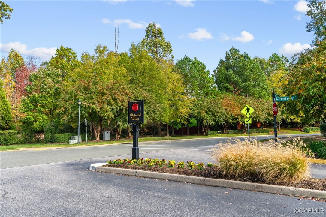 a sign board with flower plants and large trees