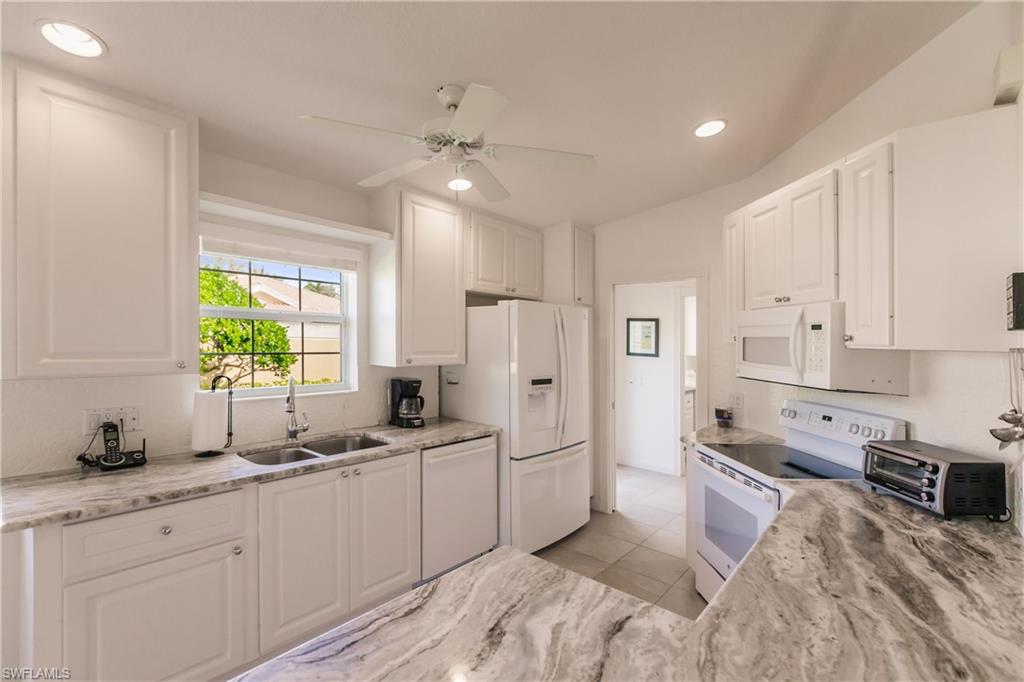 Kitchen with gorgeous granite counters, white appliances, sink, white cabinetry, ceiling fan, and light tile patterned floors