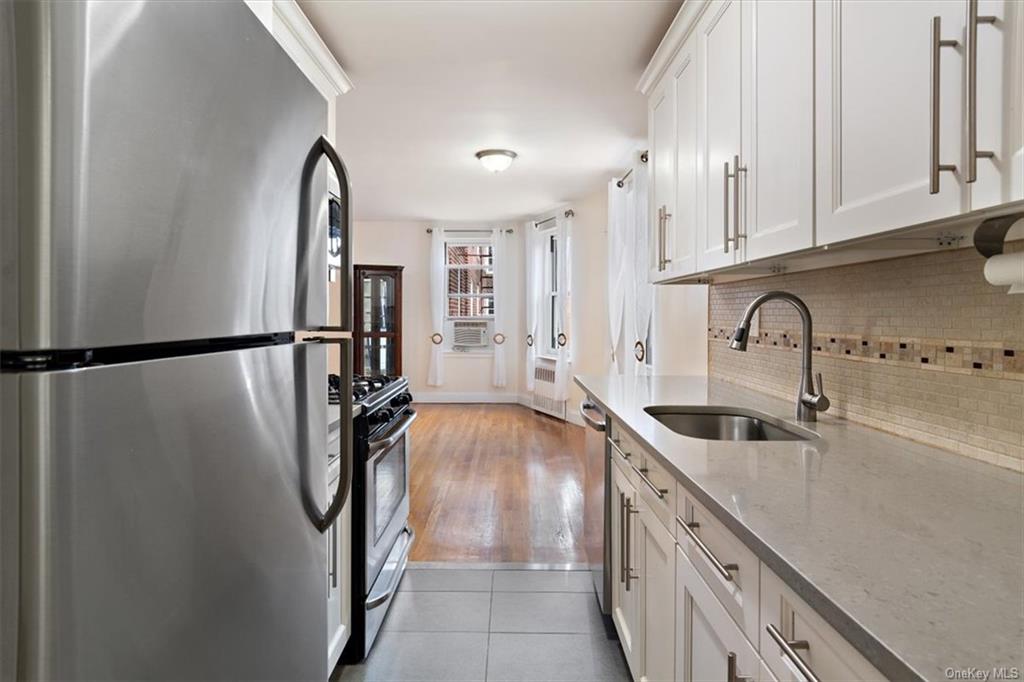 Kitchen with sink, white cabinetry, stainless steel appliances, light stone countertops, and light hardwood / wood-style floors