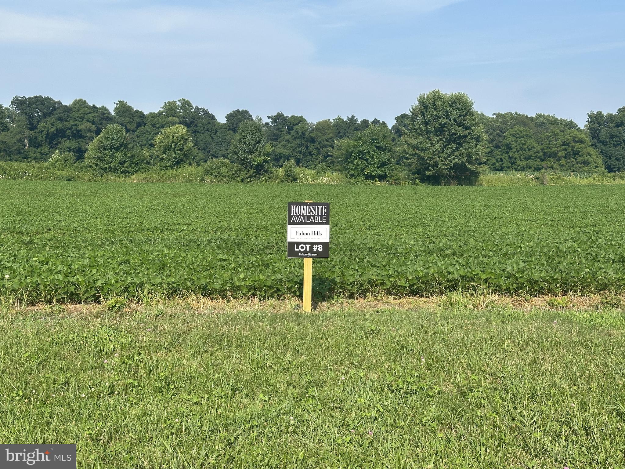 a sign board with grassy field and trees in the back