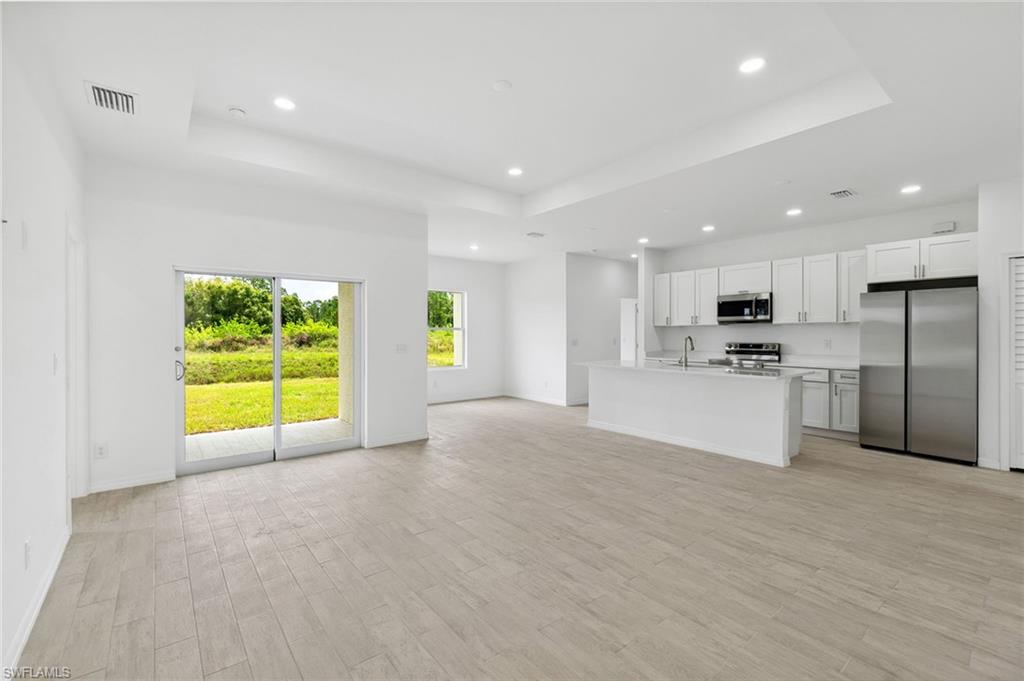 Unfurnished living room with sink, light hardwood / wood-style flooring, and a tray ceiling