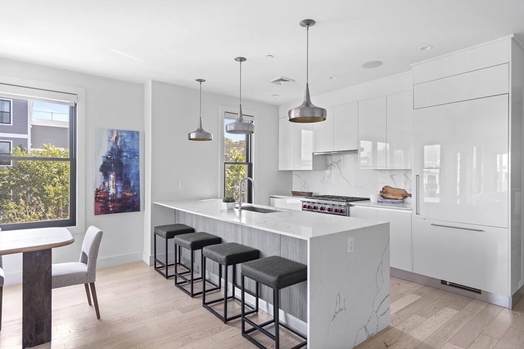 a kitchen with stainless steel appliances granite countertop a stove a refrigerator a kitchen island a dining table and chairs with wooden floor