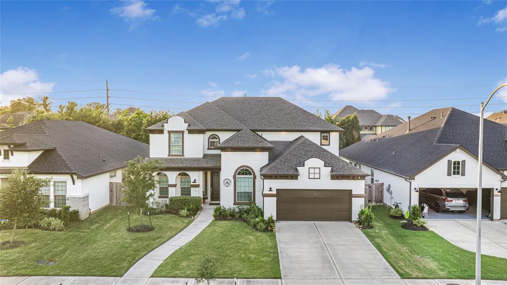 This is a spacious two-story home with a well-manicured lawn and an attached two-car garage. It features a mix of brick and stucco facade with contrasting dark roofing, and is situated in a neat suburban neighborhood.