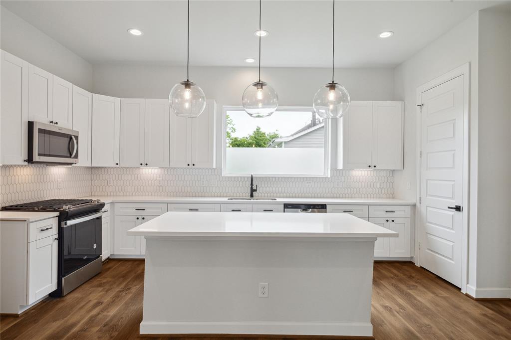 a kitchen with a sink a stove a refrigerator and white cabinets with wooden floor