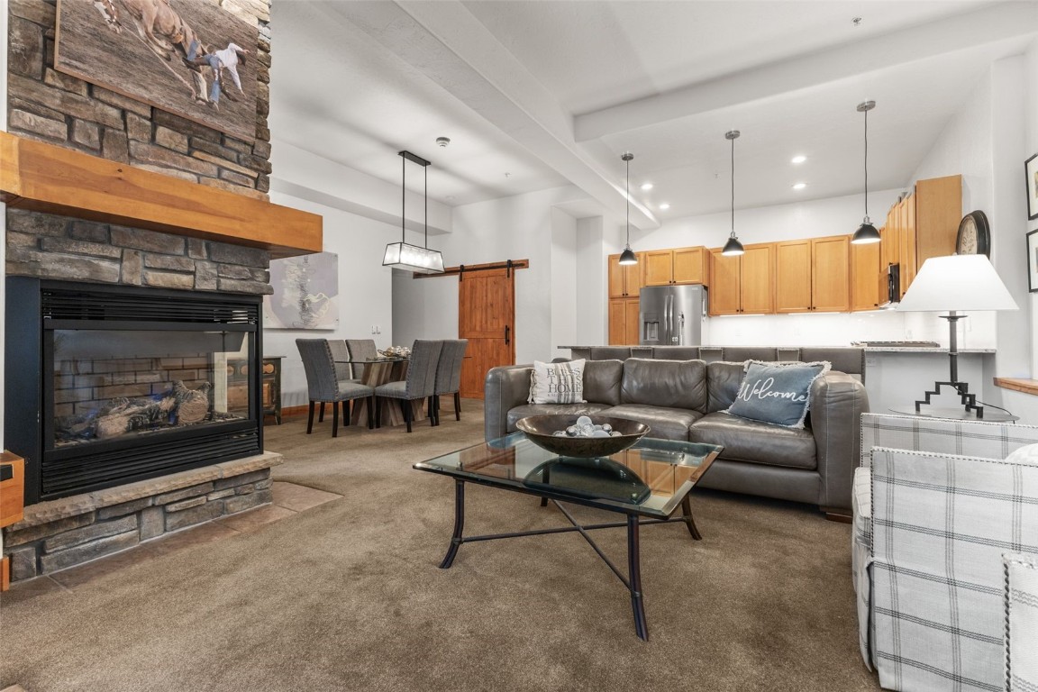 Living room with dark colored carpet, a barn door, and a stone fireplace