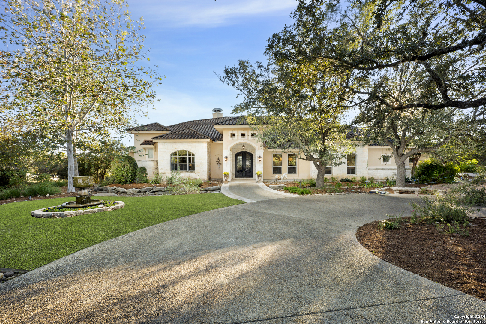 a white house with a big yard plants and large trees