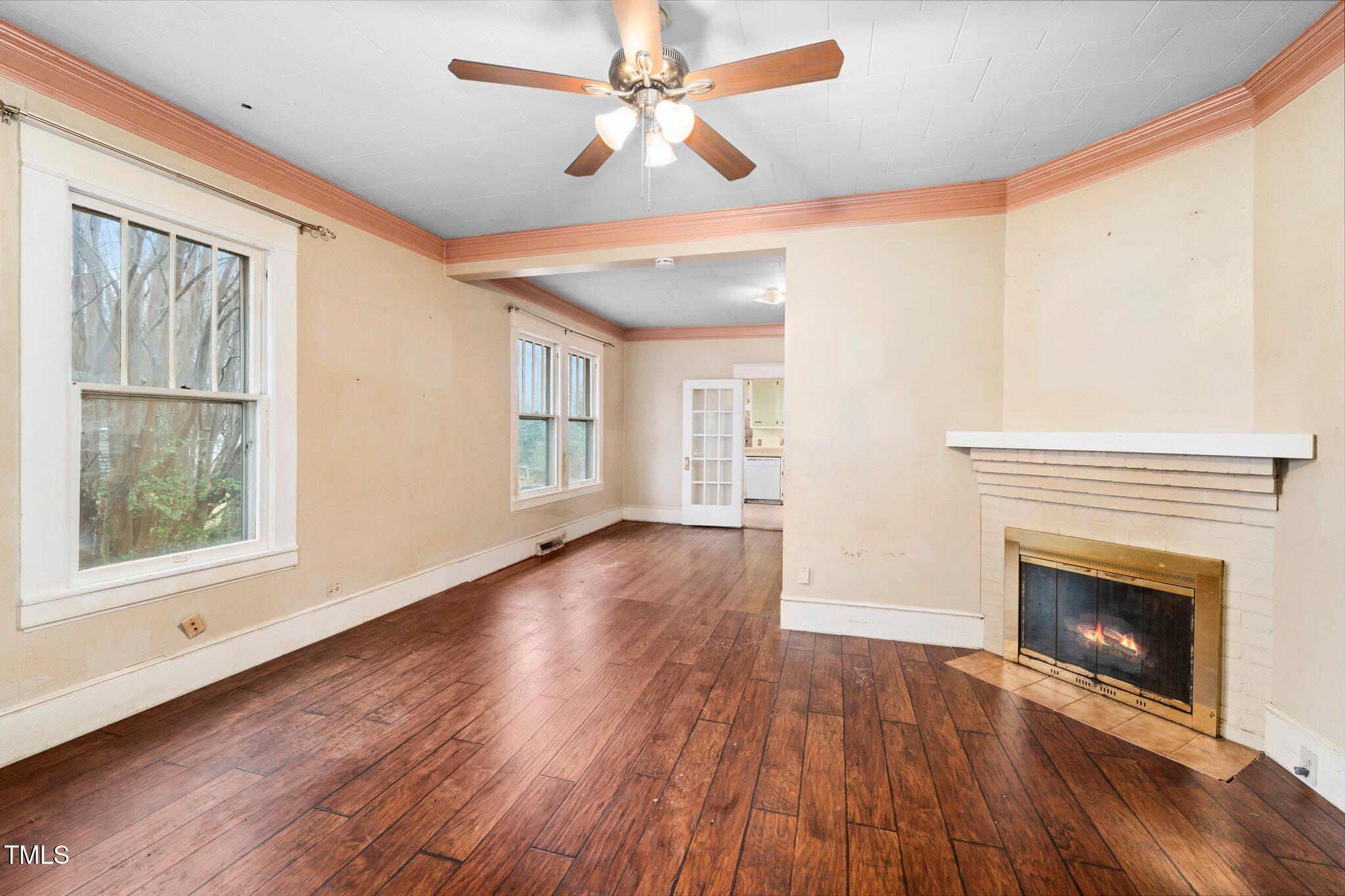 a view of an empty room with wooden floor fireplace and a window