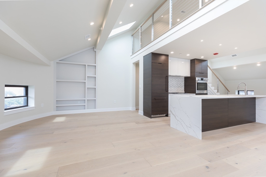 a view of an empty room with kitchen and window