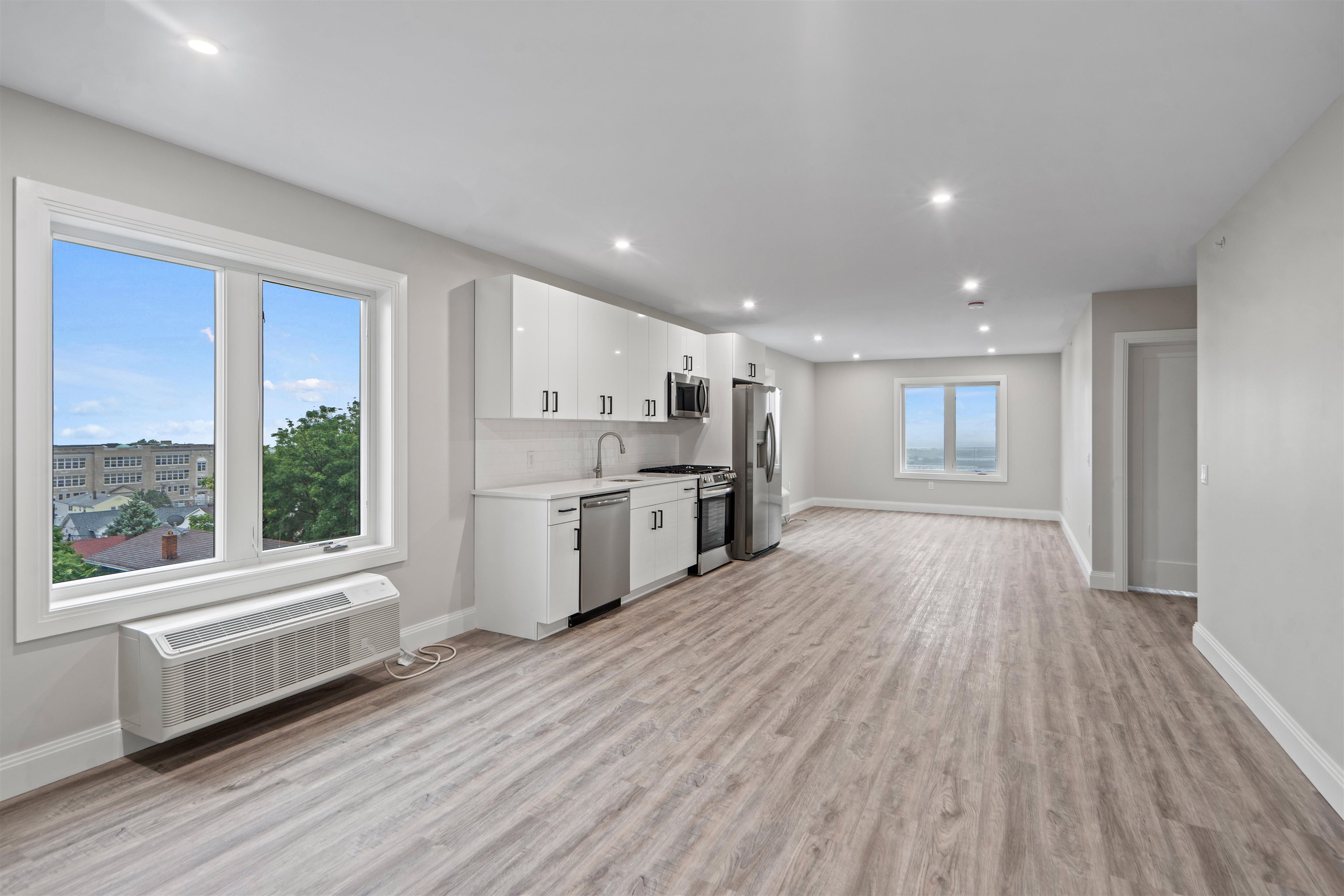 a large white kitchen with stainless steel appliances wooden floors and large window