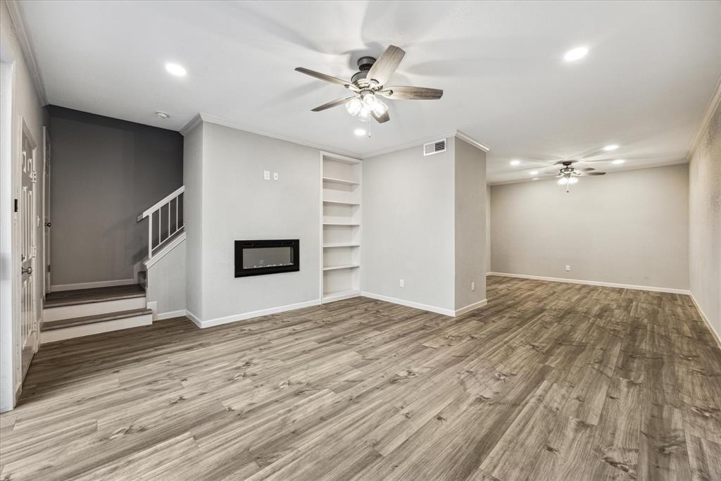 a view of an empty room with wooden floor and a ceiling fan