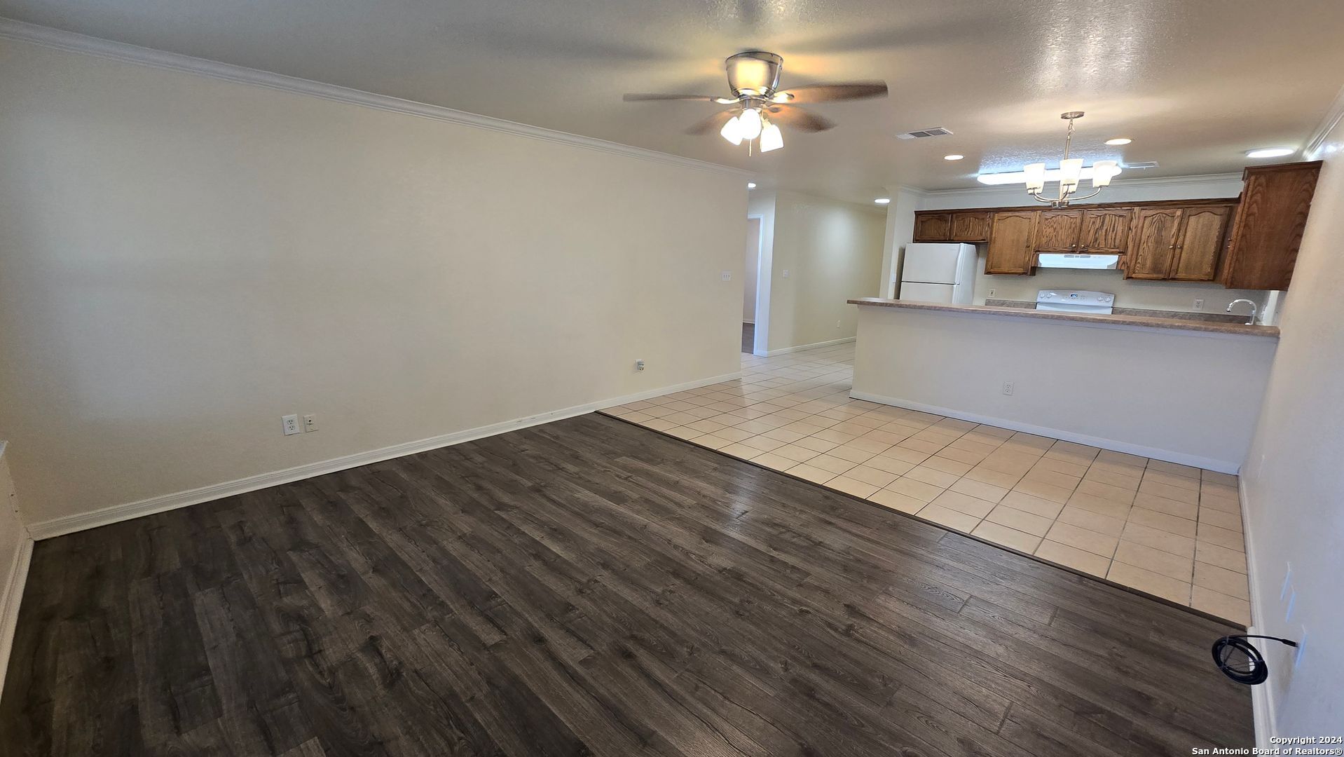 an empty room with wooden floor and kitchen view