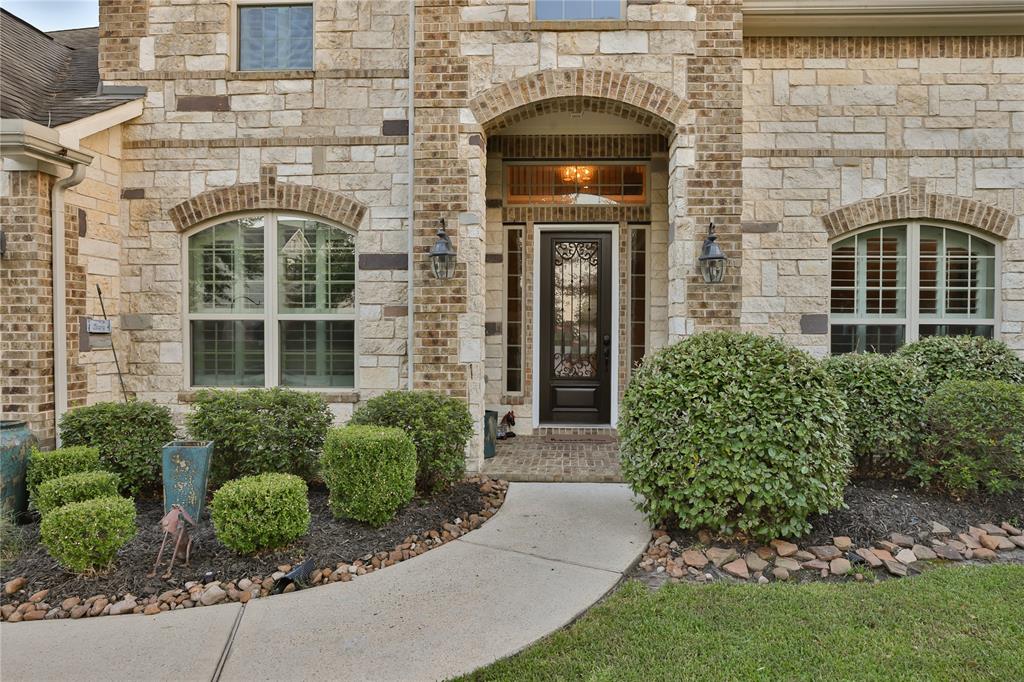 This is a well-maintained home featuring a stone facade, arched entryway with an ornate door, and manicured landscaping.