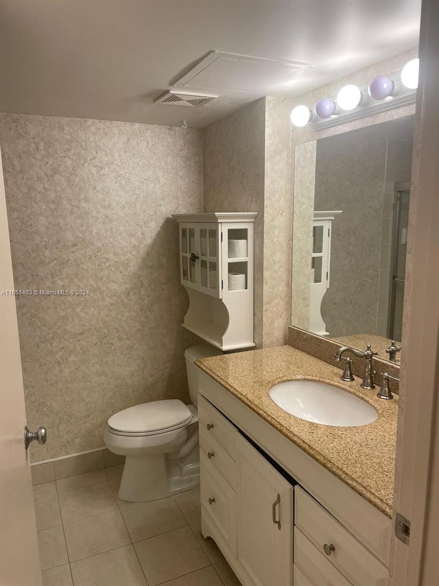 a bathroom with a granite countertop sink a toilet a mirror and shower