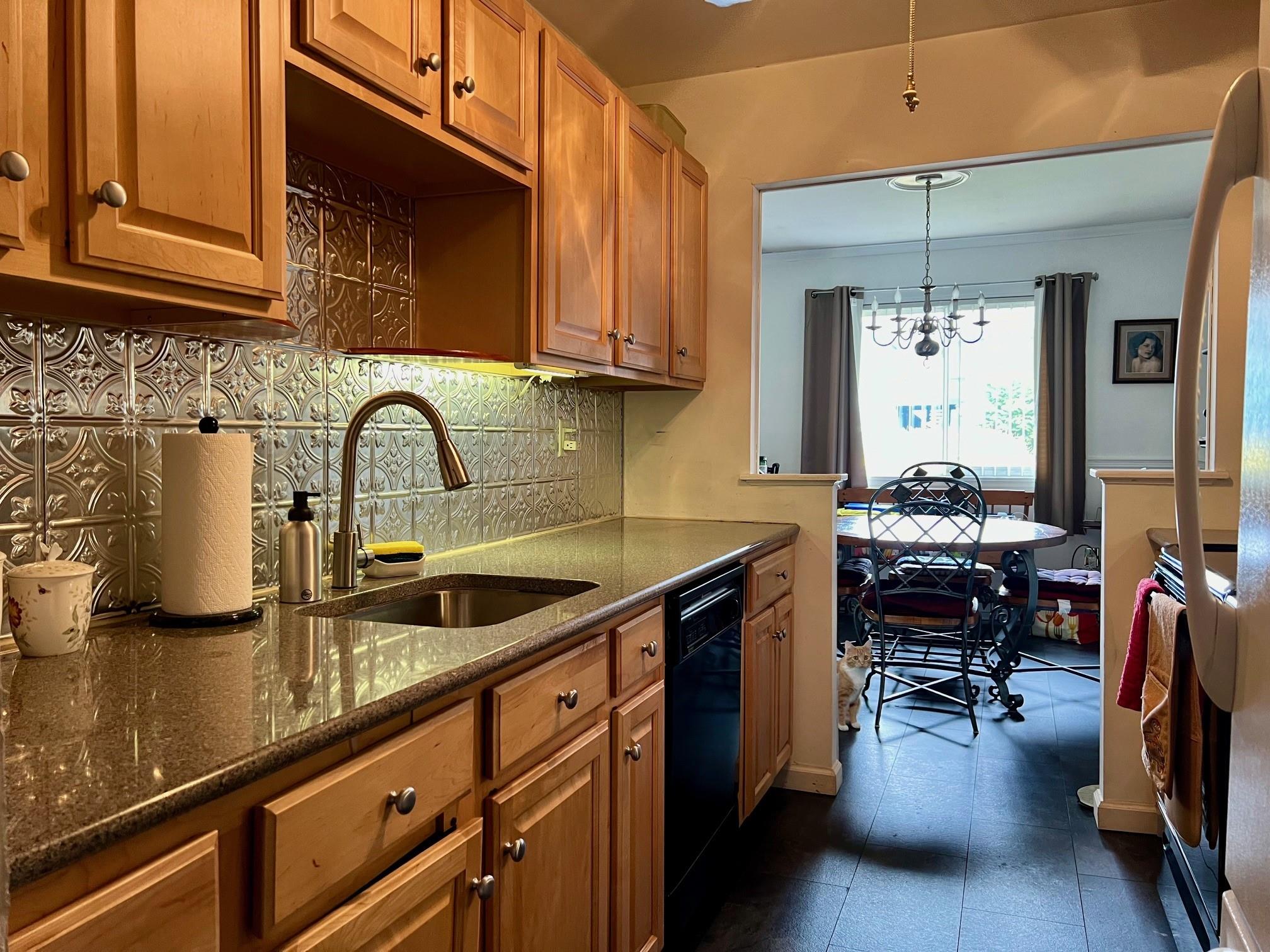 Kitchen featuring backsplash, sink, dark stone countertops, dishwasher, and hanging light fixtures