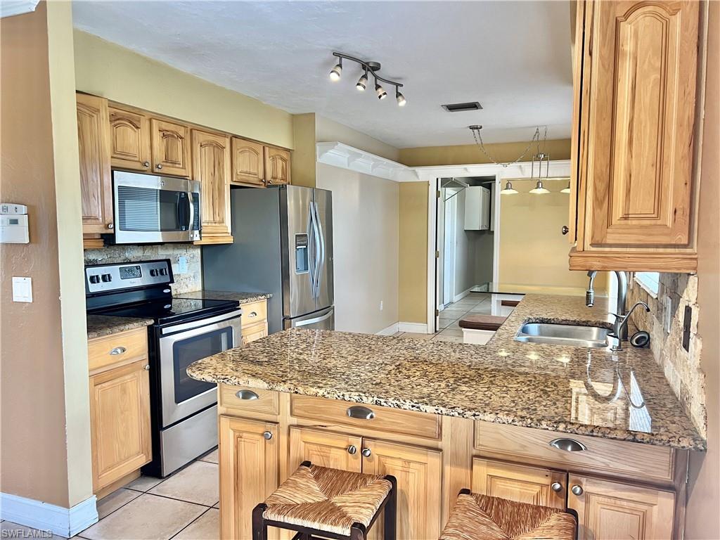 Kitchen featuring appliances with stainless steel finishes, tasteful backsplash, light stone counters, sink, and light tile patterned flooring