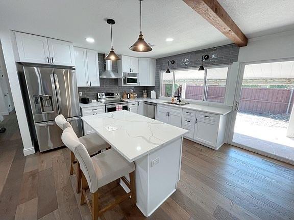 a kitchen with stainless steel appliances a stove a sink a refrigerator a center island and a wooden floor