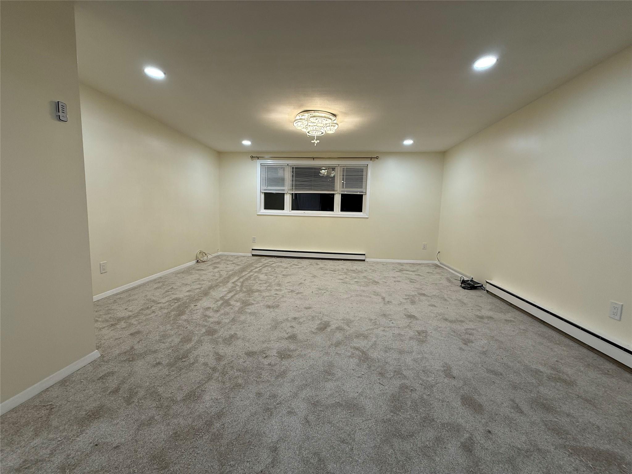 Carpeted spare room featuring a baseboard heating unit