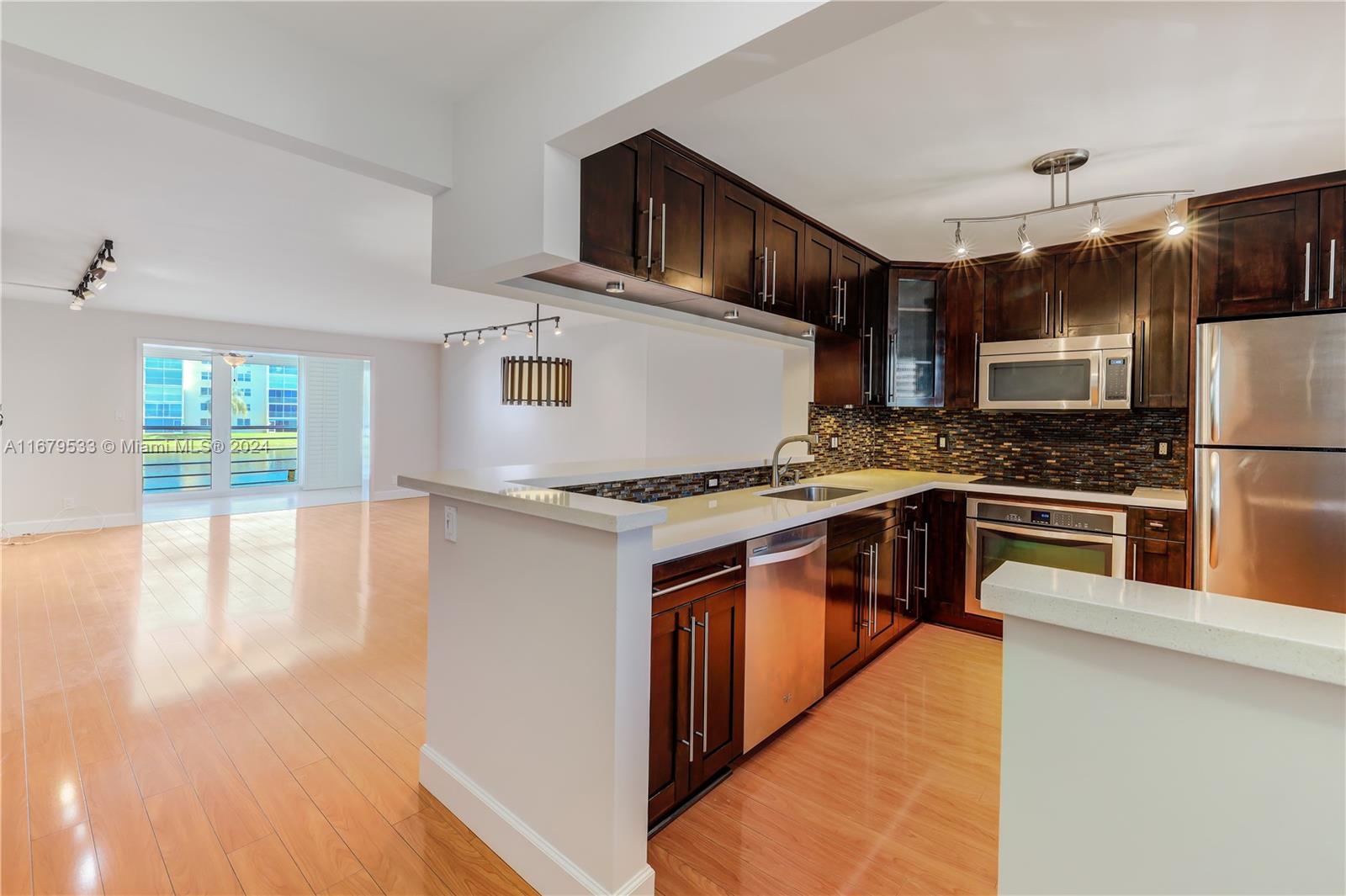 a kitchen with stainless steel appliances granite countertop a stove top oven a sink dishwasher a refrigerator and white cabinets with wooden floor