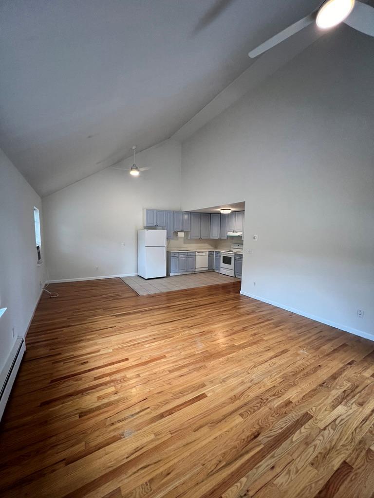 Unfurnished living room with light hardwood / wood-style flooring, baseboard heating, and high vaulted ceiling