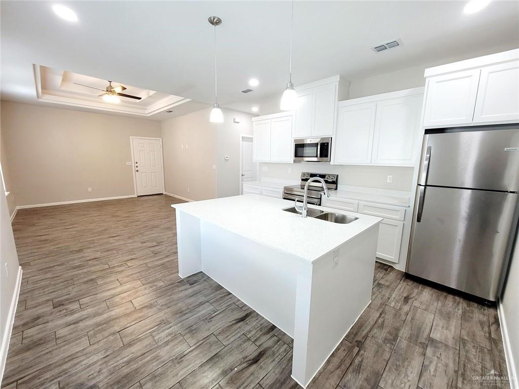 Kitchen with sink, a center island with sink, white cabinets, and appliances with stainless steel finishes