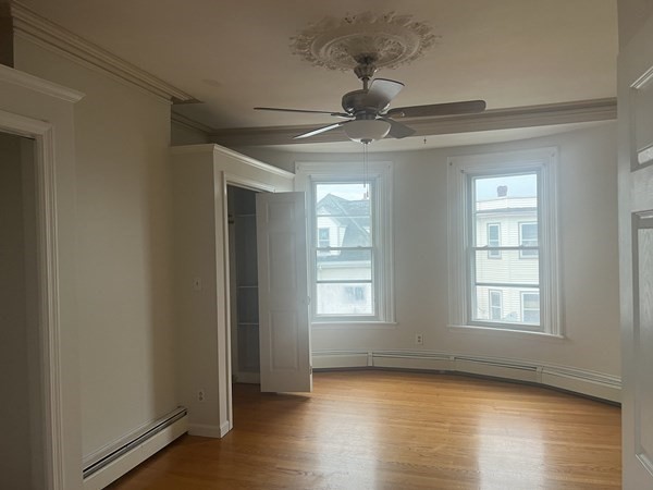 a view of an empty room with wooden floor and fan