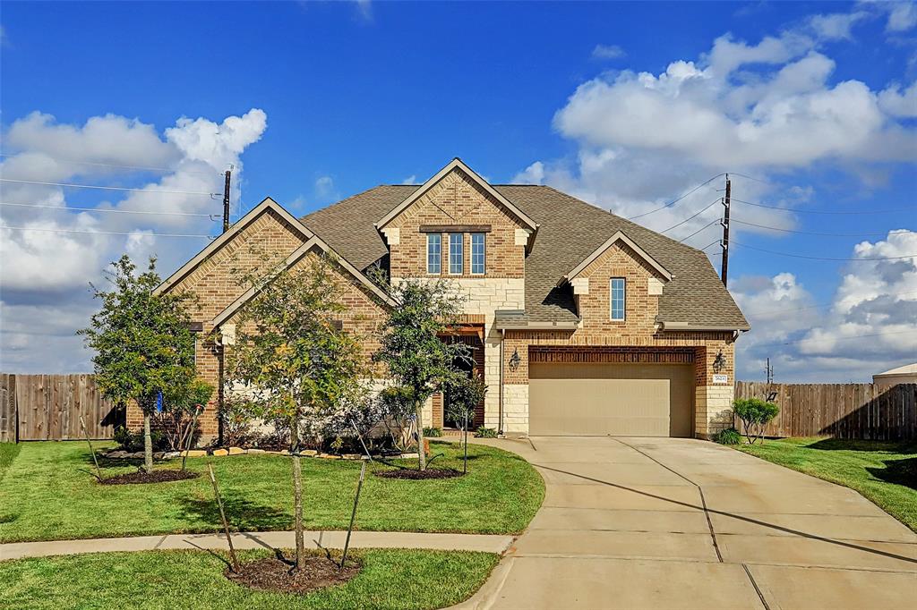 This is a two-story, brick-façade home featuring a well-manicured lawn, an attached two-car garage, and a sizable driveway. It's situated under a clear blue sky, giving the property a bright and inviting appearance