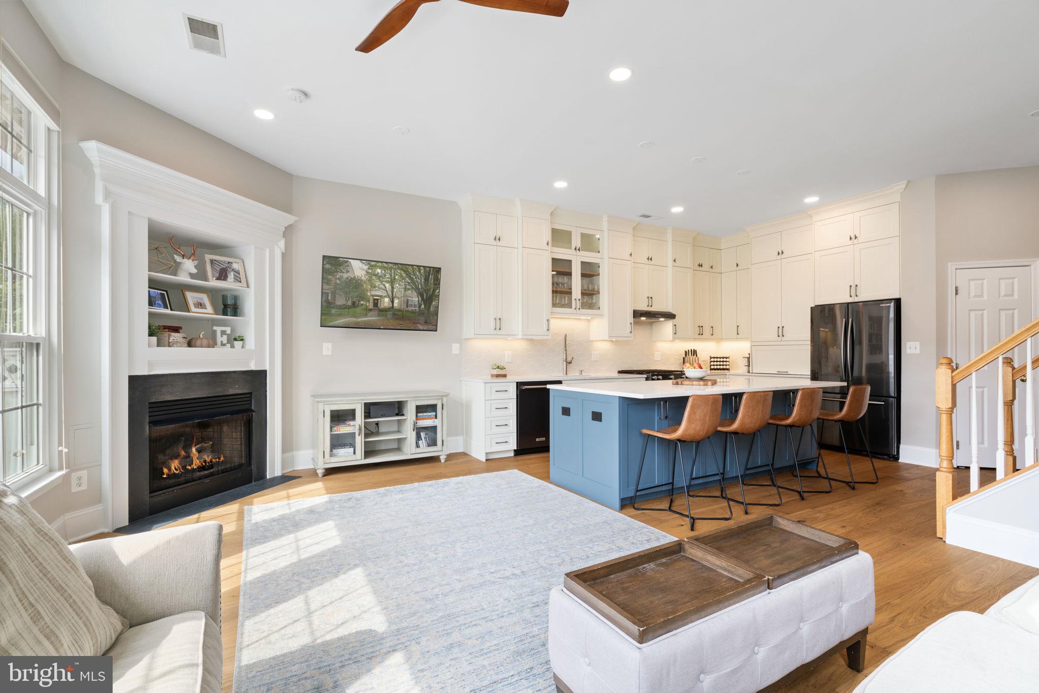 a living room with stainless steel appliances furniture a fireplace a rug kitchen view and a window