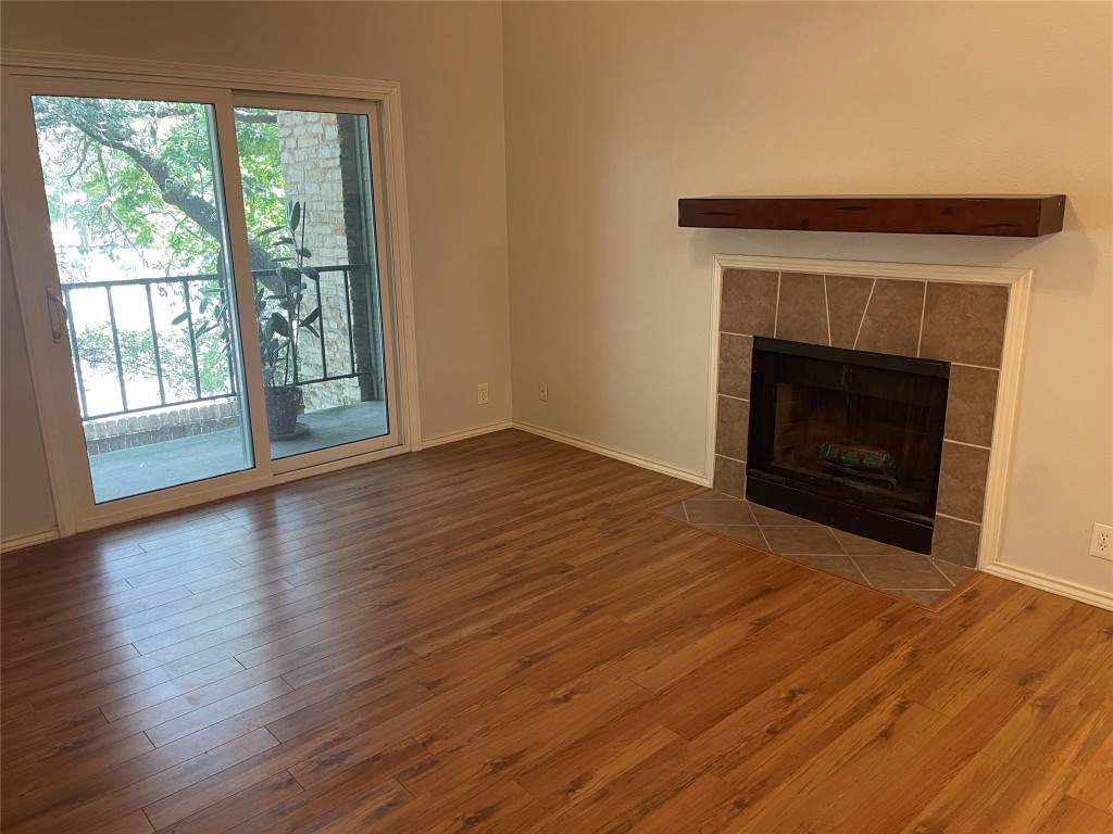 a view of an empty room with wooden floor fireplace and a window