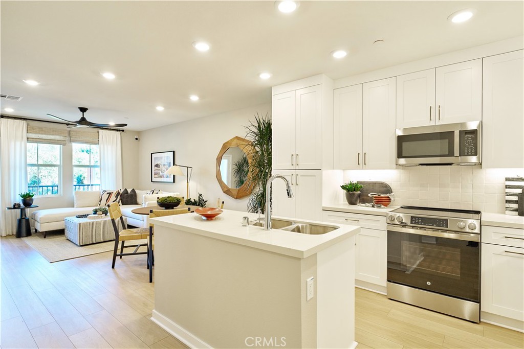 a open kitchen with stainless steel appliances kitchen island granite countertop a stove a sink a refrigerator and white cabinets with wooden floor