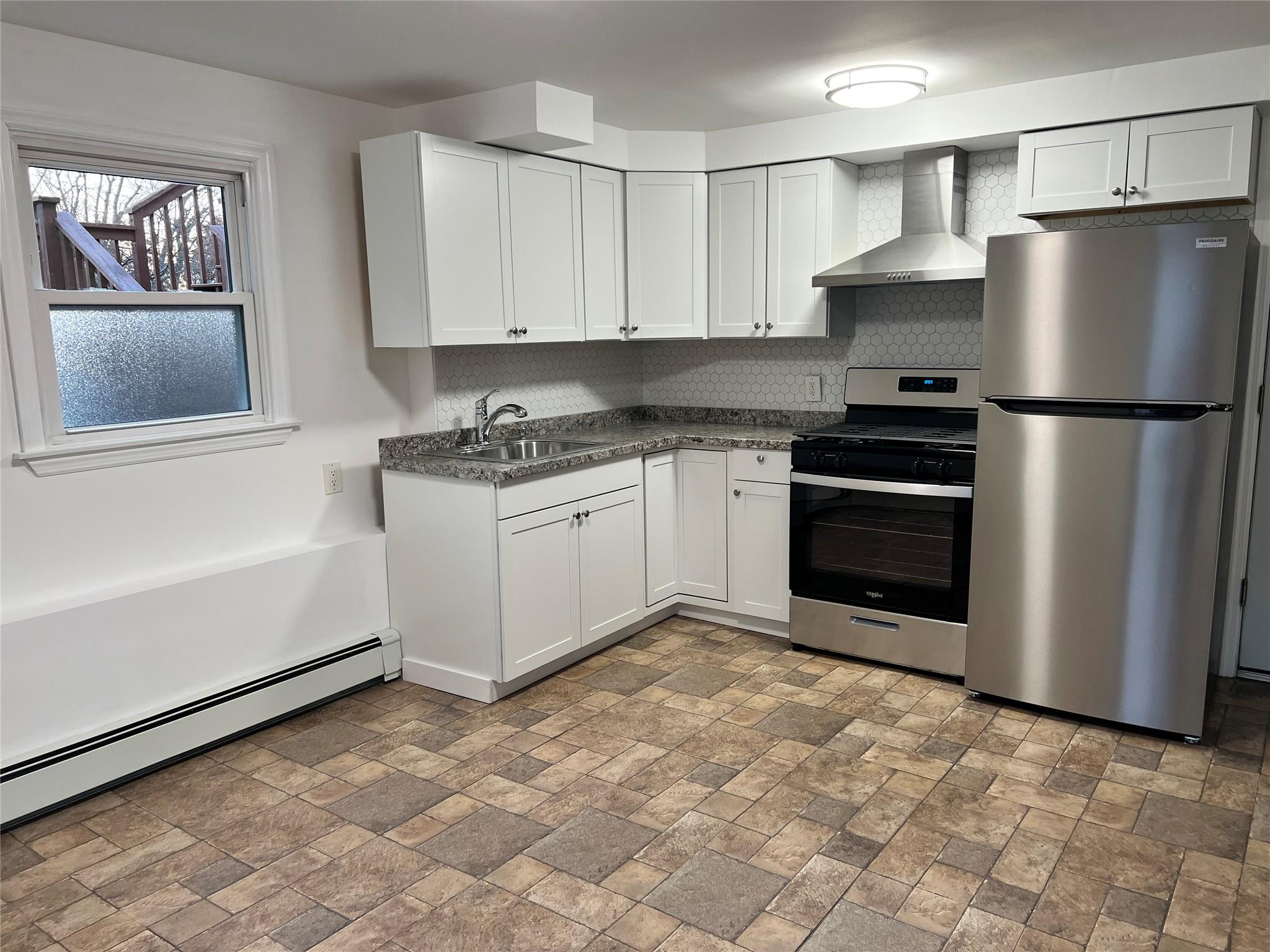 Kitchen with white cabinets, sink, stainless steel appliances, and wall chimney range hood